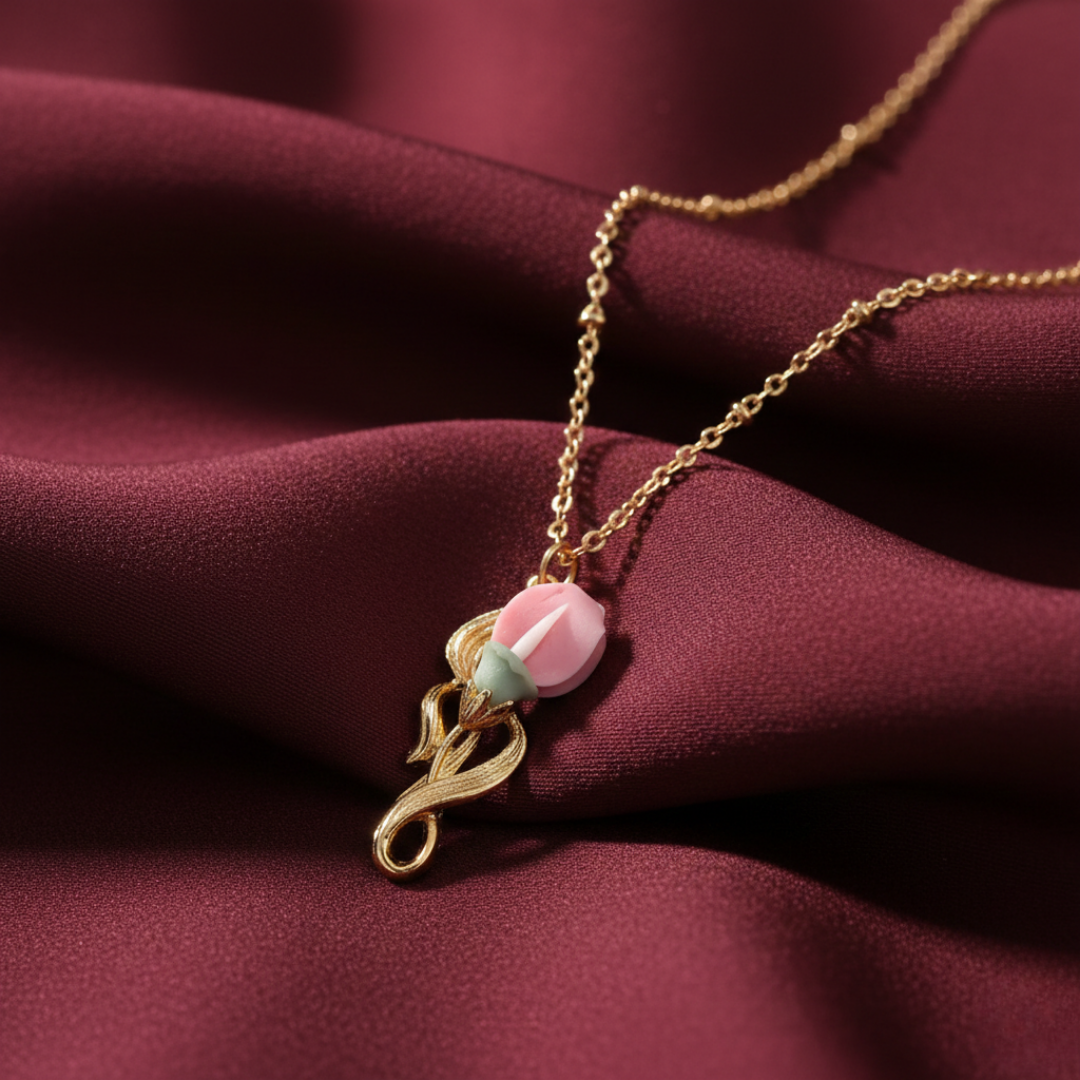Gold necklace with a rose pink floral pendant on a red fabric.