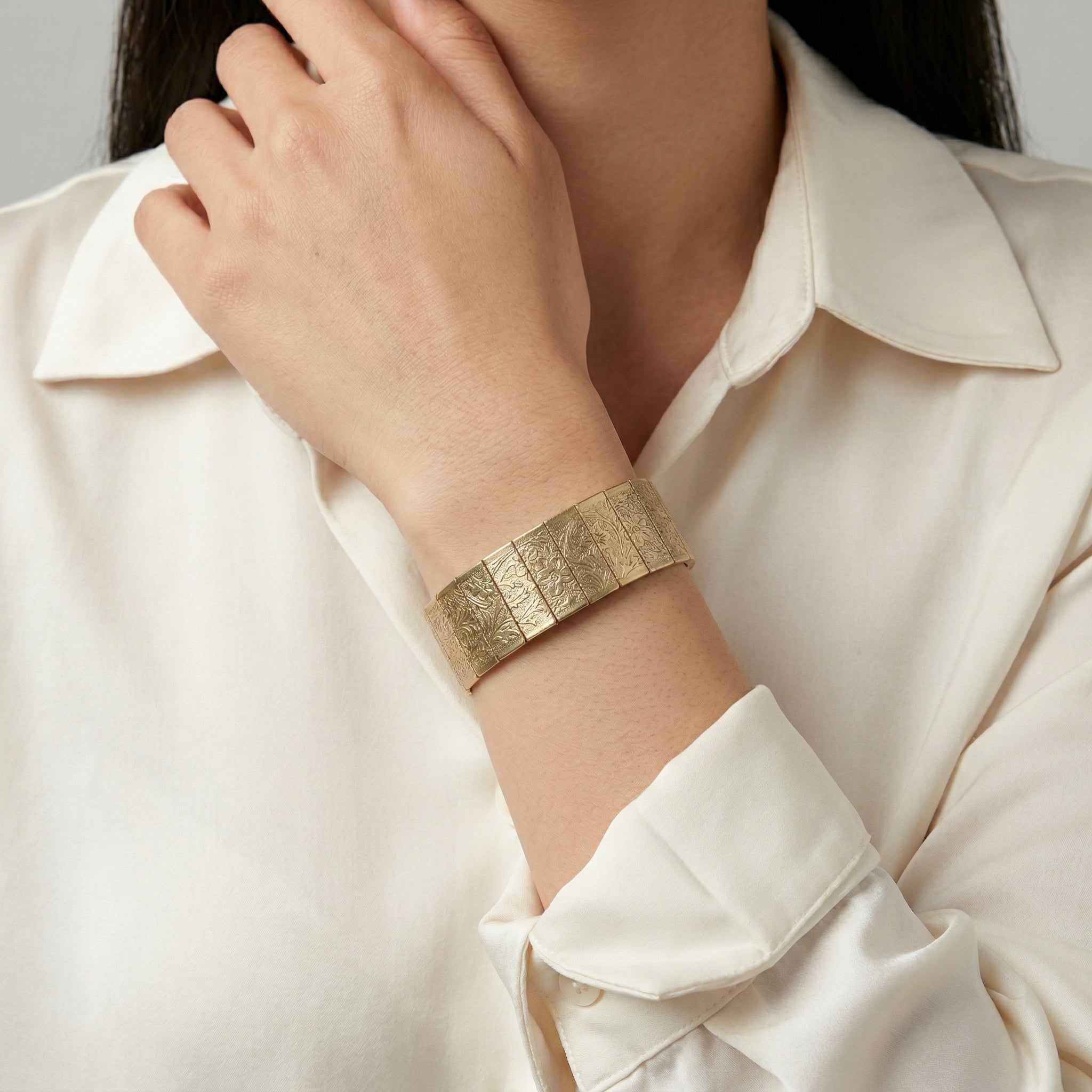 Gold floral bracelet on a person wearing a white shirt