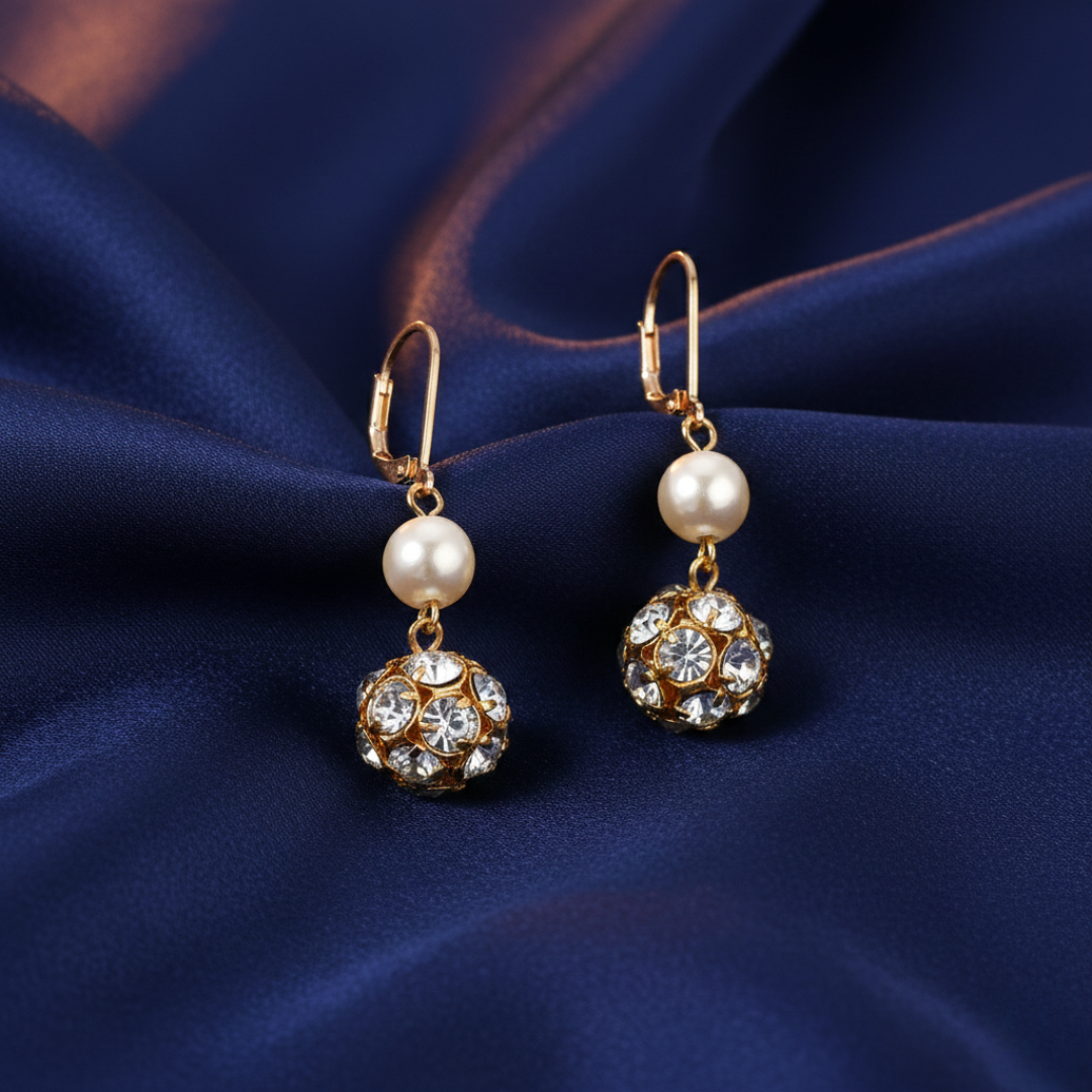 Gold earrings with faux pearls and crystals on a dark blue fabric background