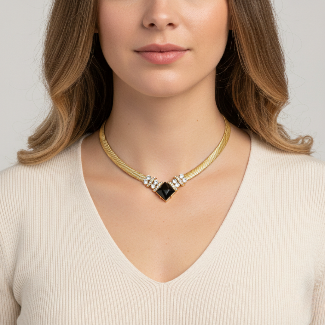 Woman wearing a gold necklace with a black pendant on a plain background