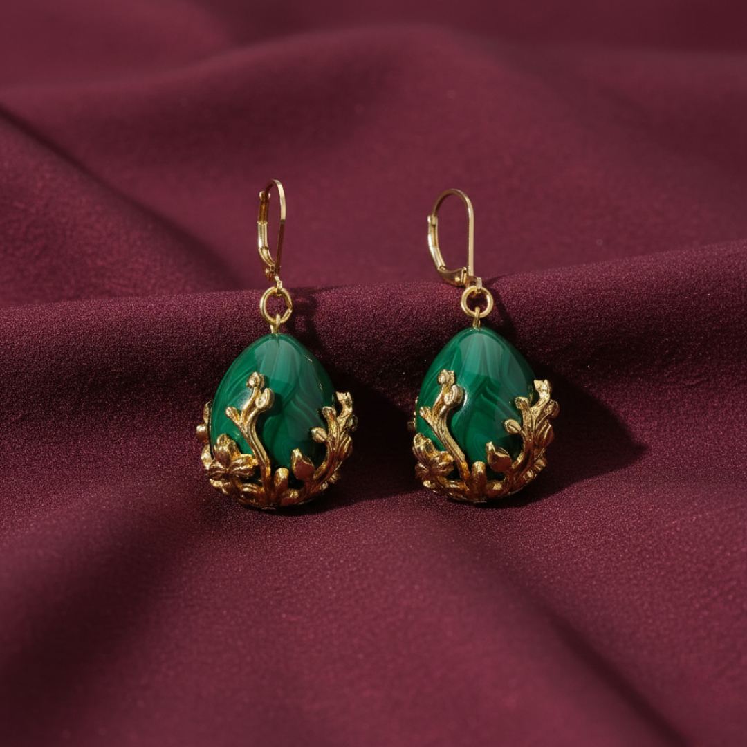 Pair of green teardrop earrings with gold accents on a purple fabric