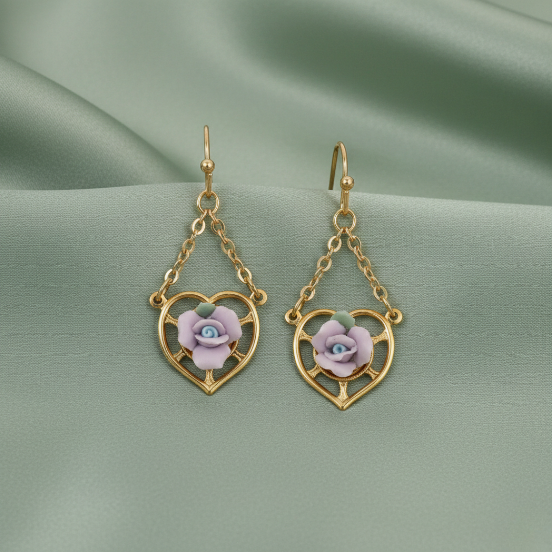 Gold heart-shaped earrings with floral designs on a green fabric background