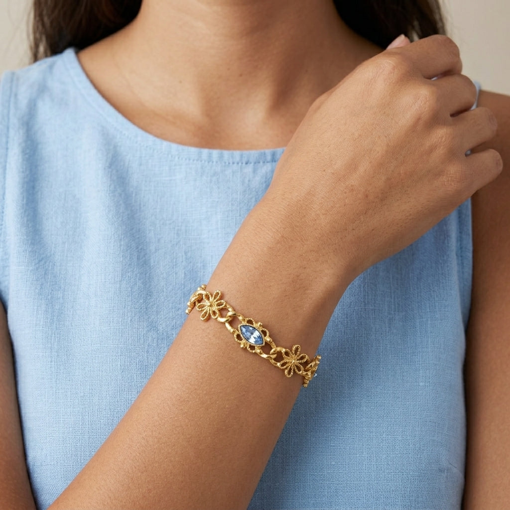 Gold bracelet with a light blue sapphire crystal on a person wearing a light blue dress.