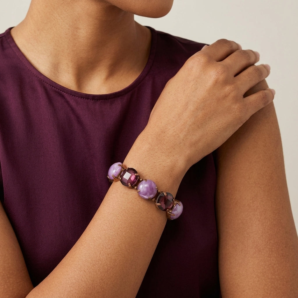 Person wearing a bracelet with purple beads and gemstones on a plain background
