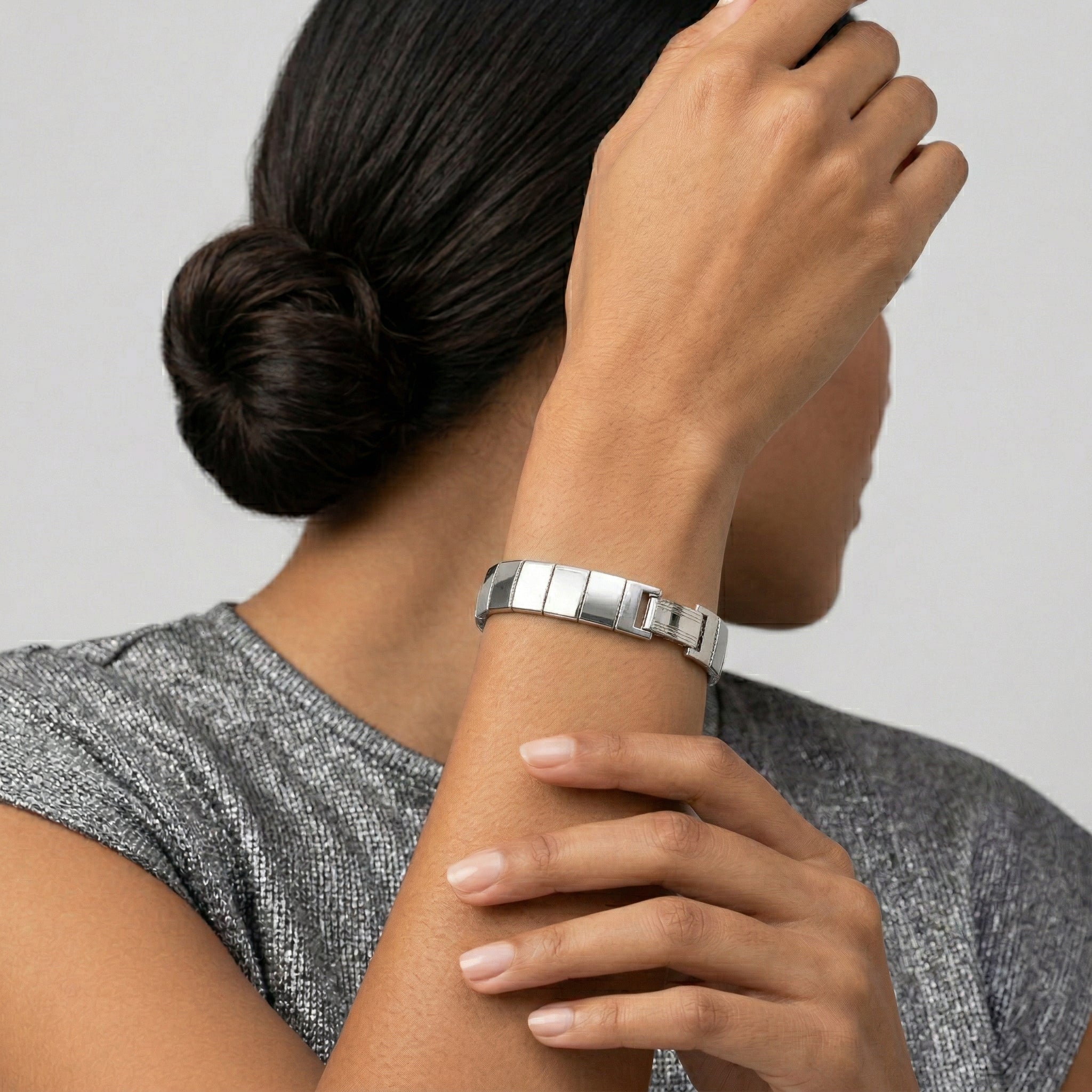 Person wearing a silver bracelet on a plain background