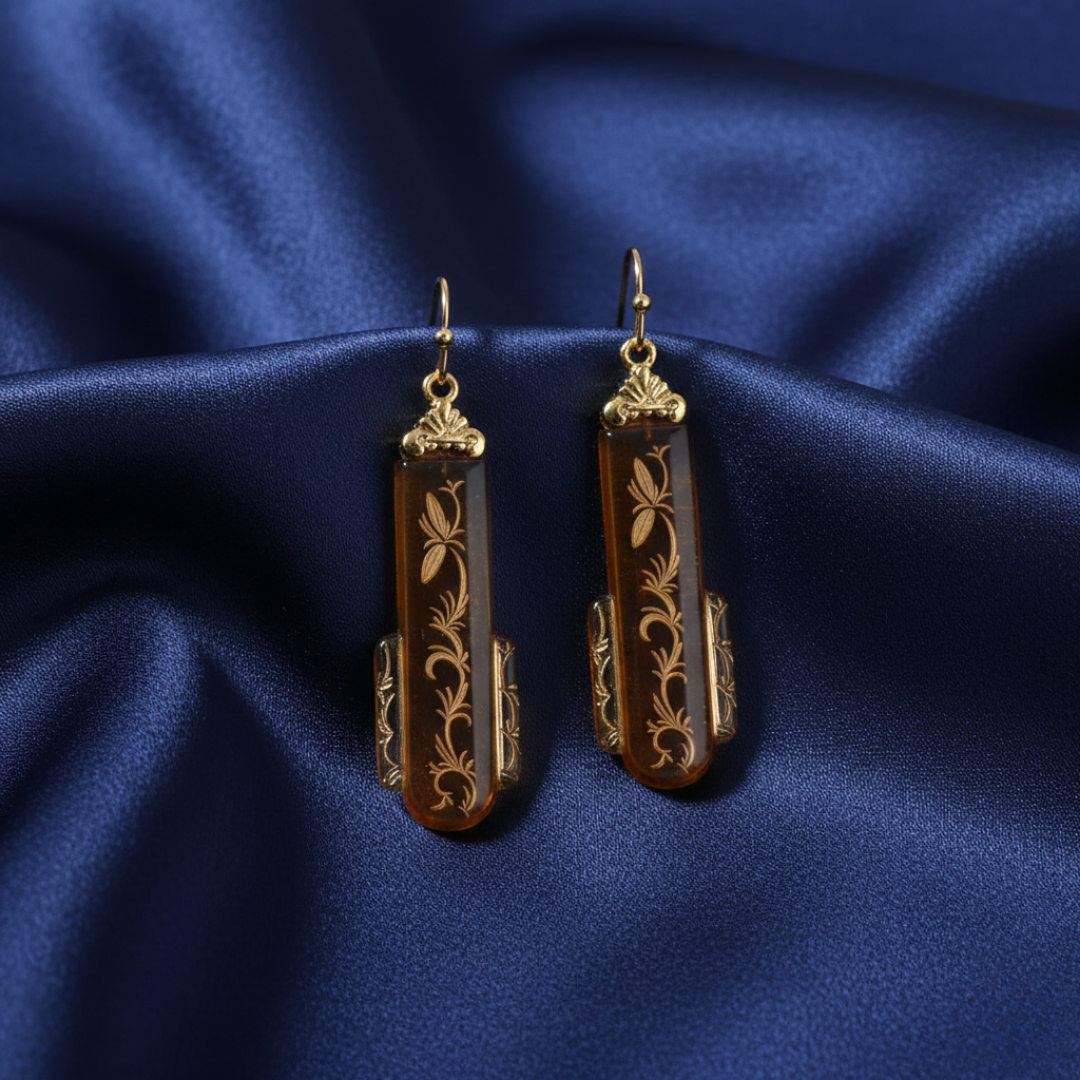 Pair of gold and brown glass earrings on a blue satin background