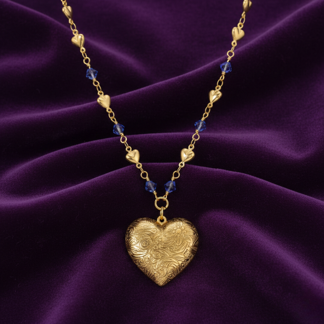 Gold heart-shaped necklace with blue beads on a purple fabric background