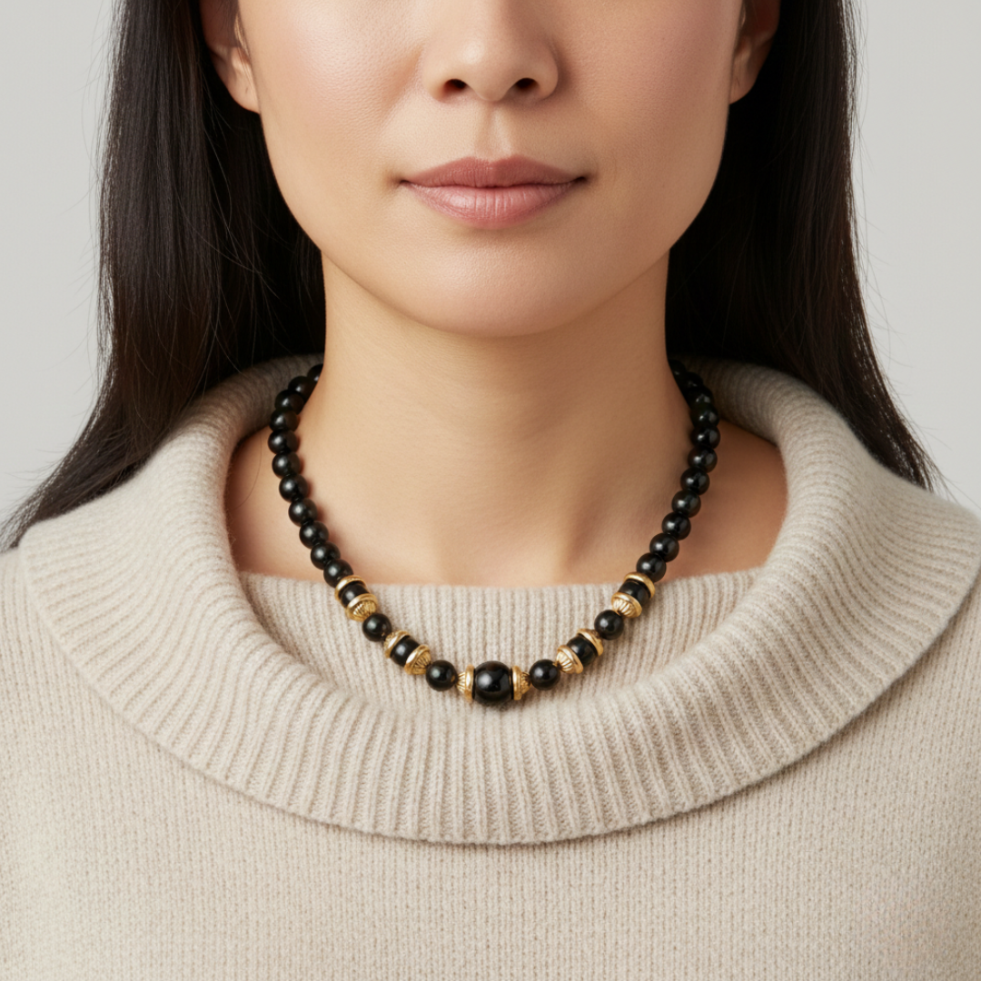 Woman wearing a black and gold beaded necklace against a neutral background