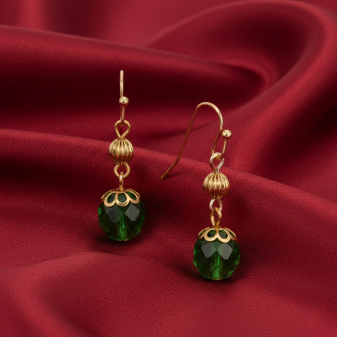Gold earrings with green crystals on a red fabric background