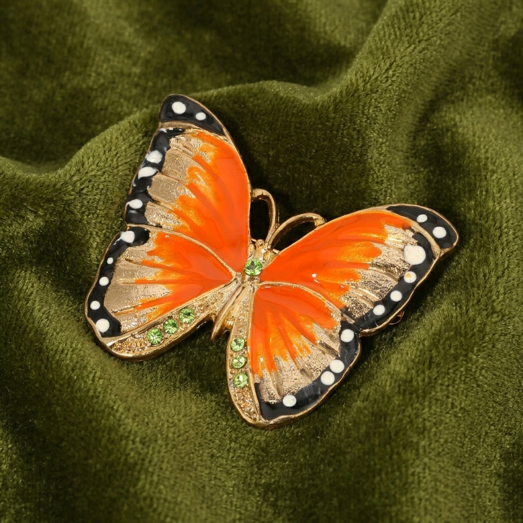 Butterfly-shaped brooch with orange and black wings on a green fabric background