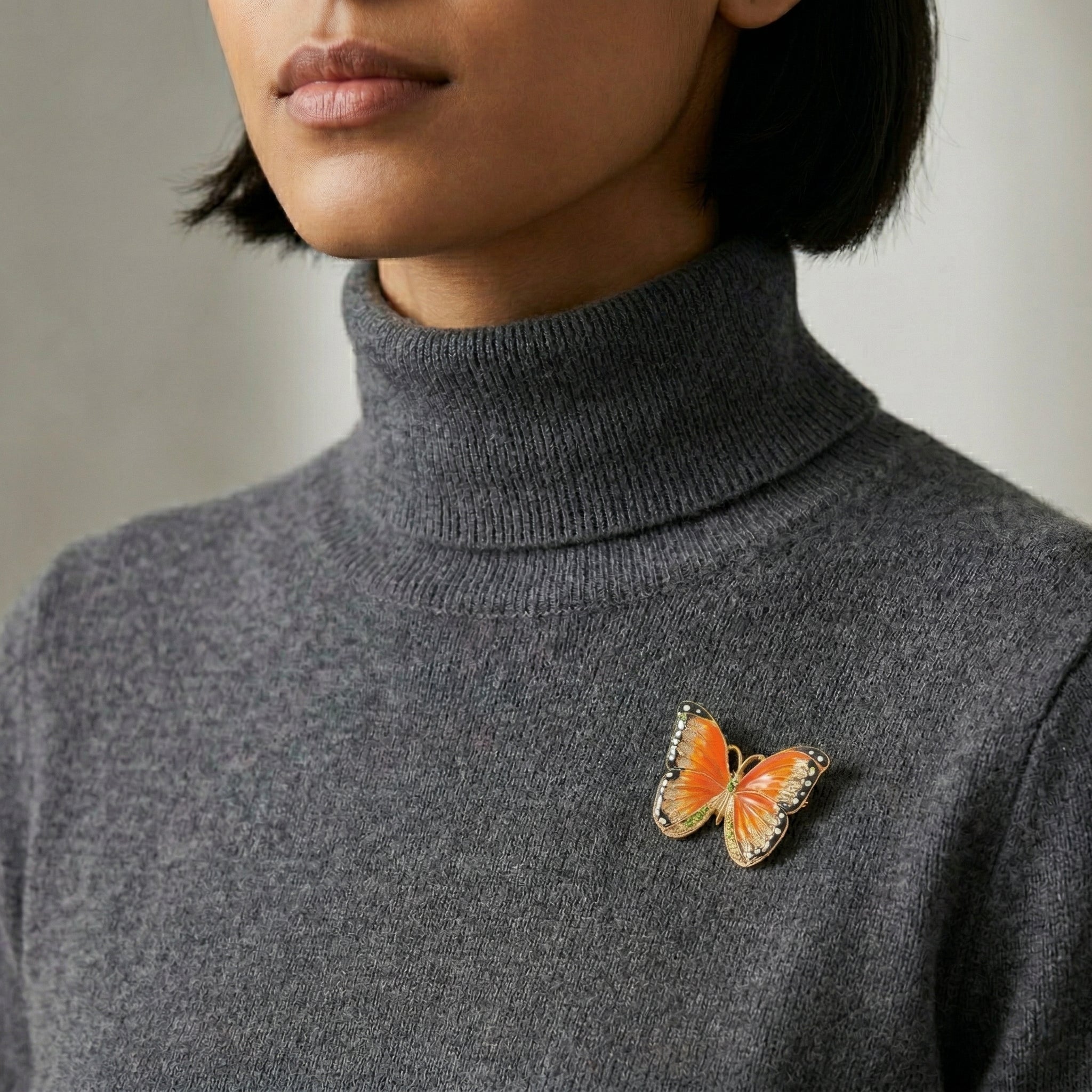 Person wearing a gray turtleneck sweater with a butterfly brooch.