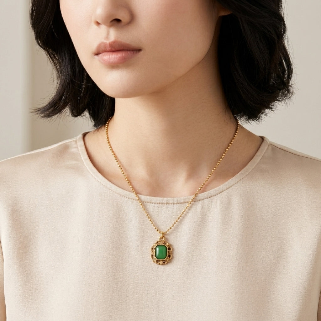Woman wearing a gold necklace with a green gemstone pendant against a neutral background