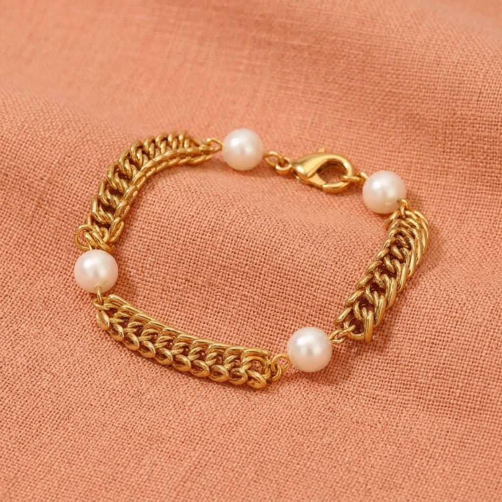 Gold tone link bracelet with white faux pearls resting on peach colored linen