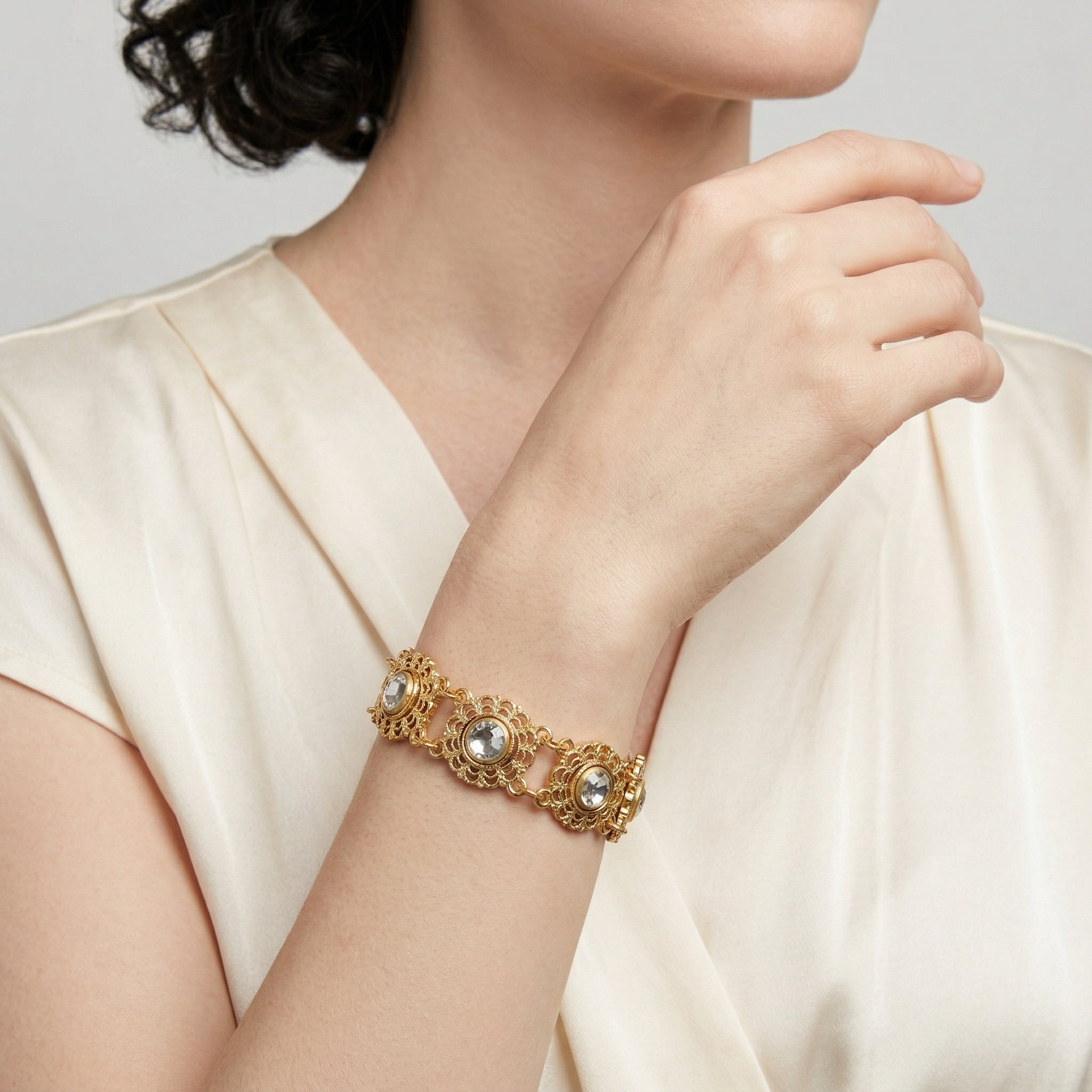 Woman wearing a gold bracelet with clear crystals on a neutral background
