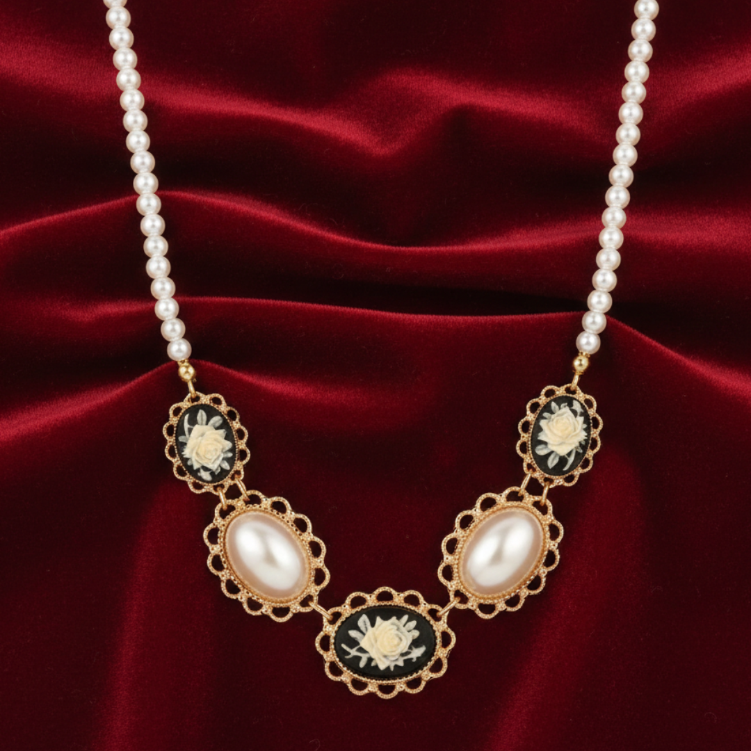 Pearl necklace with gold and black decorative cameo elements on a red fabric background.