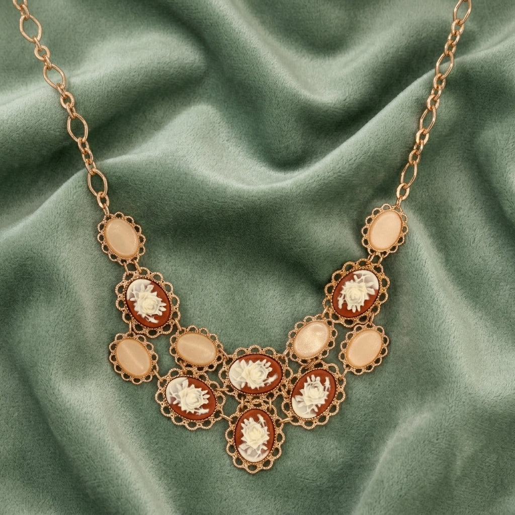 Gold tone cameo rose bib necklace with peach colored stones resting on olive green fabric