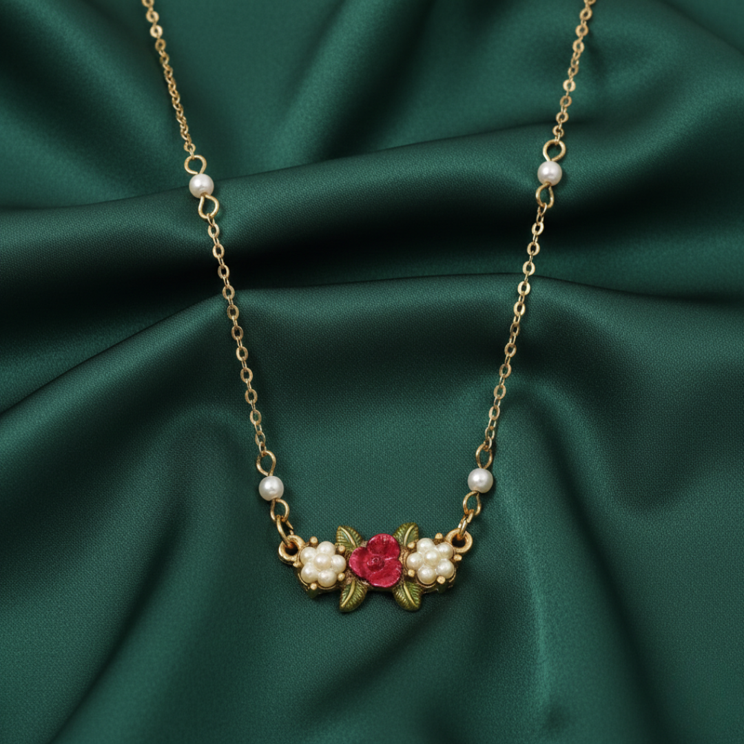 Necklace with floral design and faux pearls with a red rose on the pendant on a green fabric background