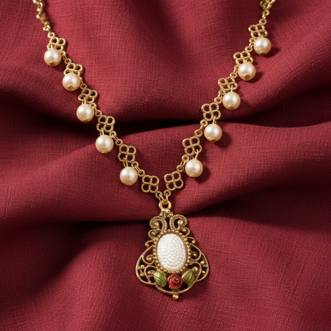 Gold necklace with pearls and a decorative pendant with a rose attached beneath on a red fabric background