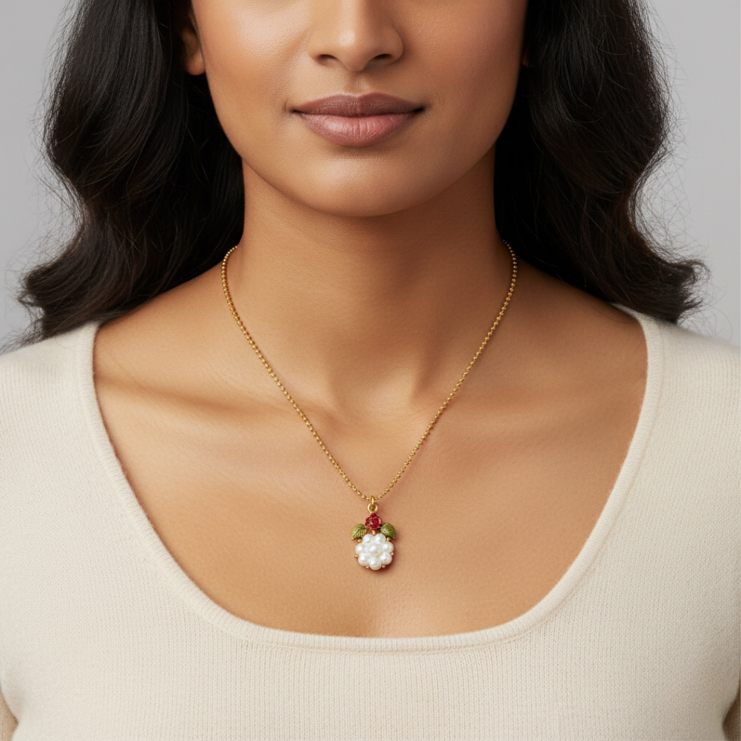 Woman wearing a gold necklace with a pearl and floral pendant against a neutral background