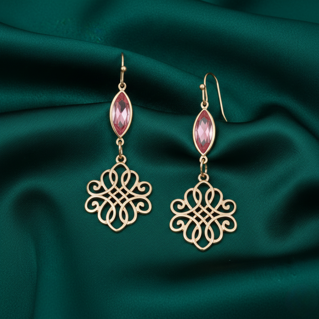 Gold earrings with rose gemstones on a green fabric background.