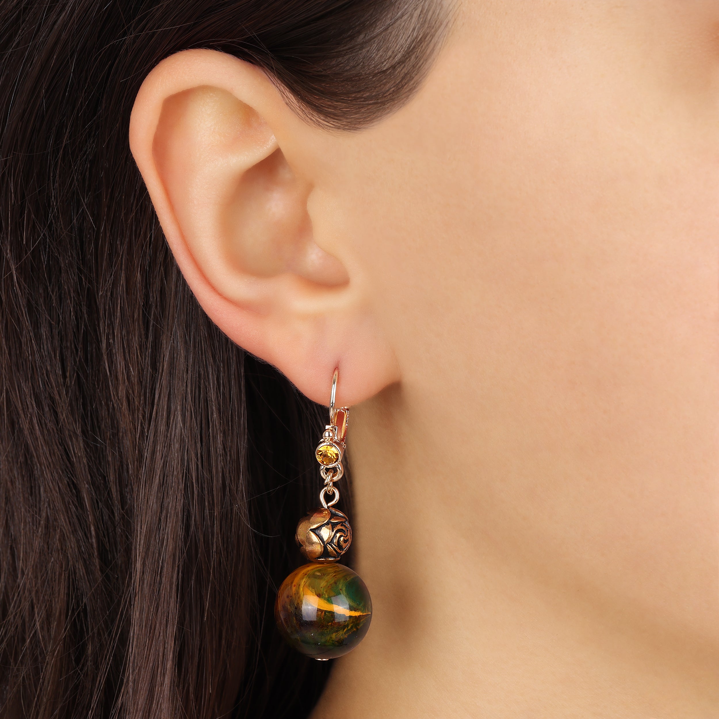 A close-up of a person's ear wearing a Round Harvest Green & Antiqued Gold Rose Bead Drop Earrings