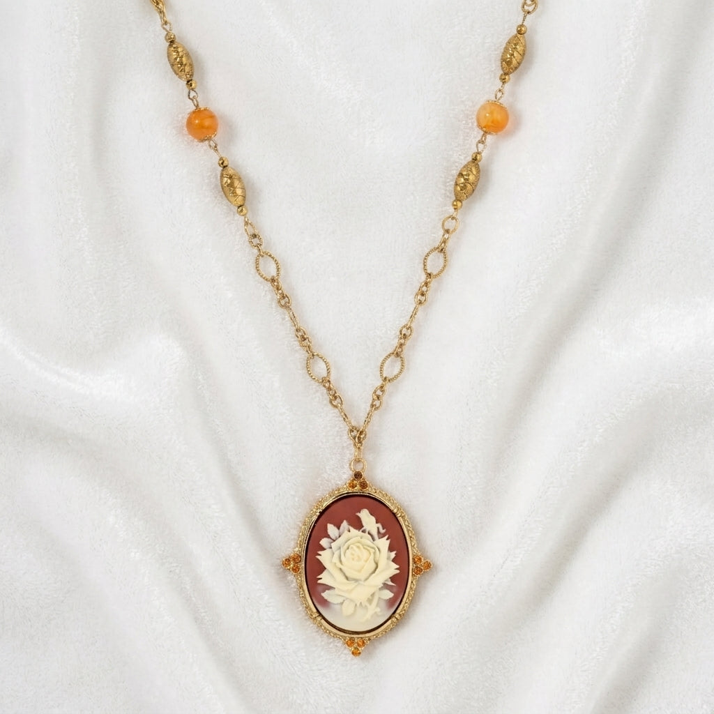 Red carnelian ivory rose pendant that has topaz stone accents on a gold tone chain resting on white satin fabric