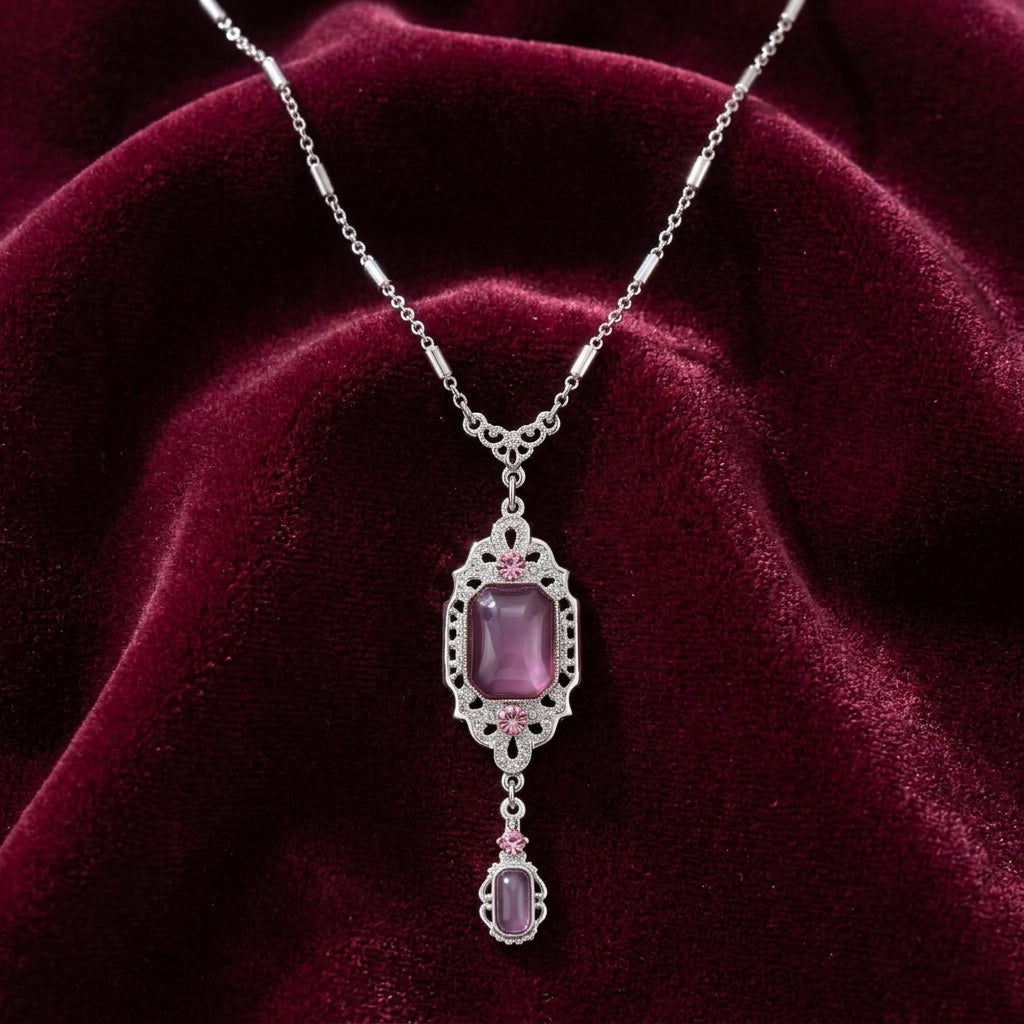 Silver tone purple stone drop pendant necklace resting on dark magenta fabric