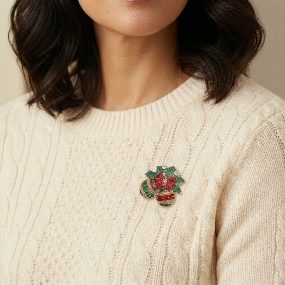 Person wearing a cream sweater with a decorative holiday ornament brooch on a neutral background