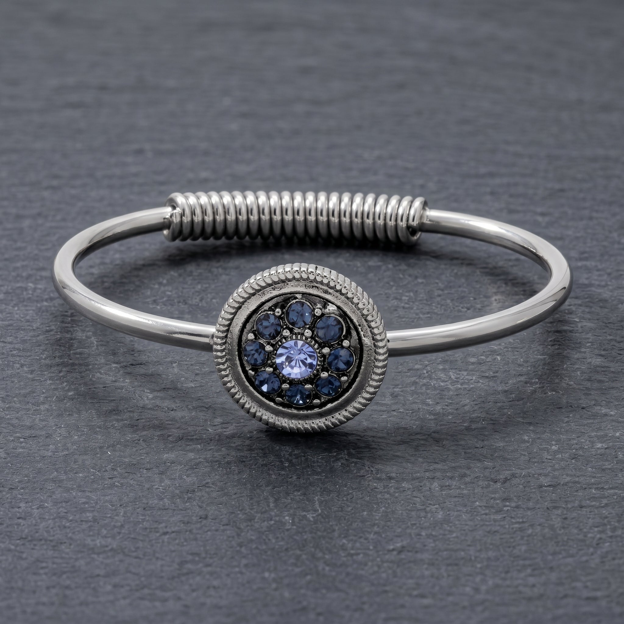 Blue pave crystal silver tone spring hinge bracelet resting on a gray stone surface