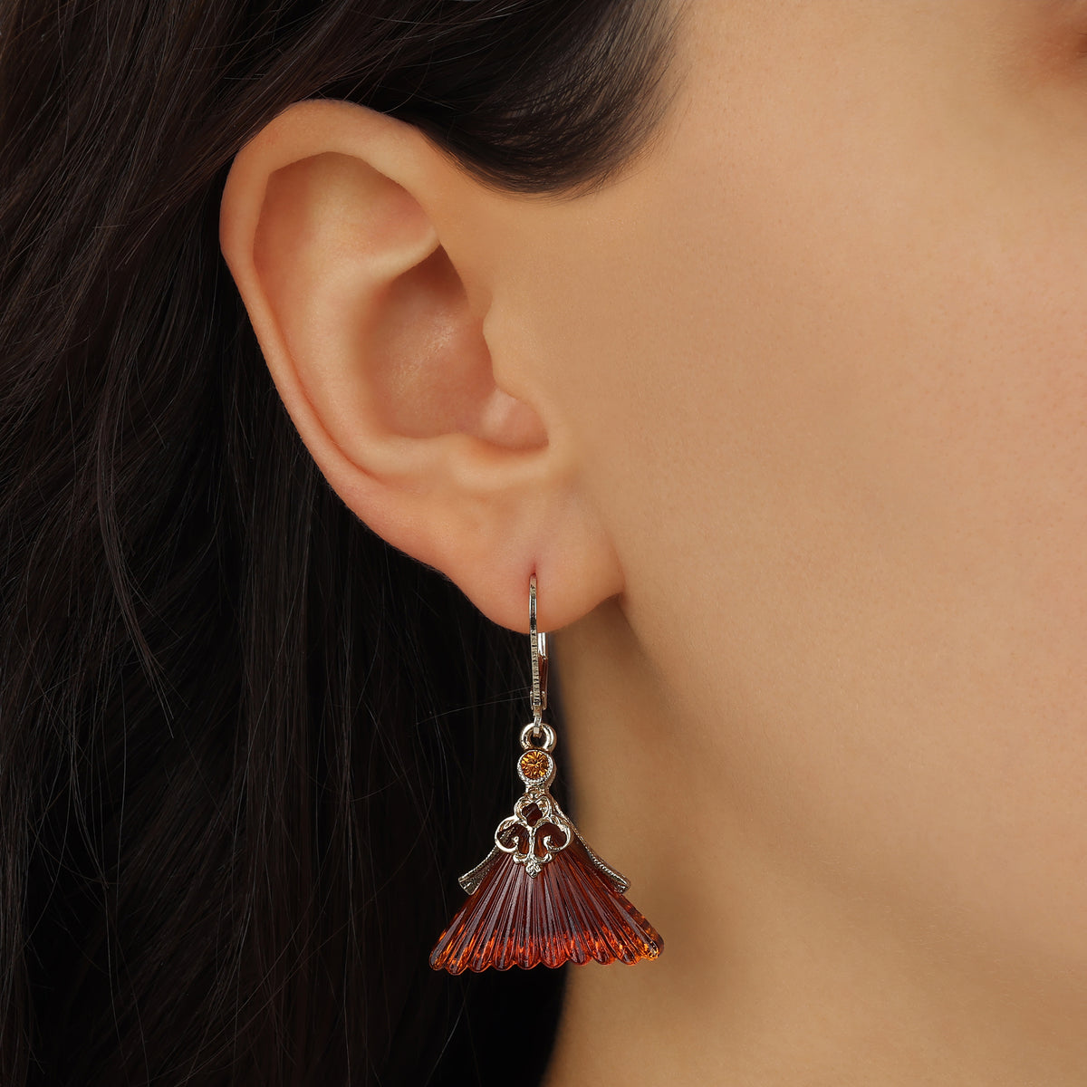A close-up of a model's ear wearing a Golden Fluted Triangle Topaz Glass & Crystal Drop Earrings