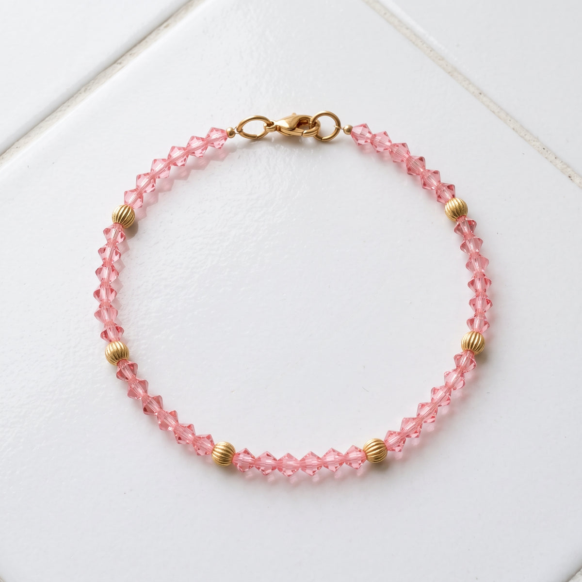 Rose Pink European Glass Lantern Crystal & Gold Beaded Bracelet resting on white tile