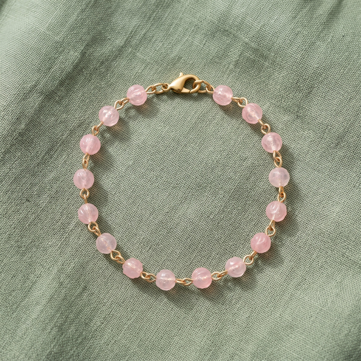 Light Rose Pink Beaded Bracelet displayed on a textured sage green fabric background.