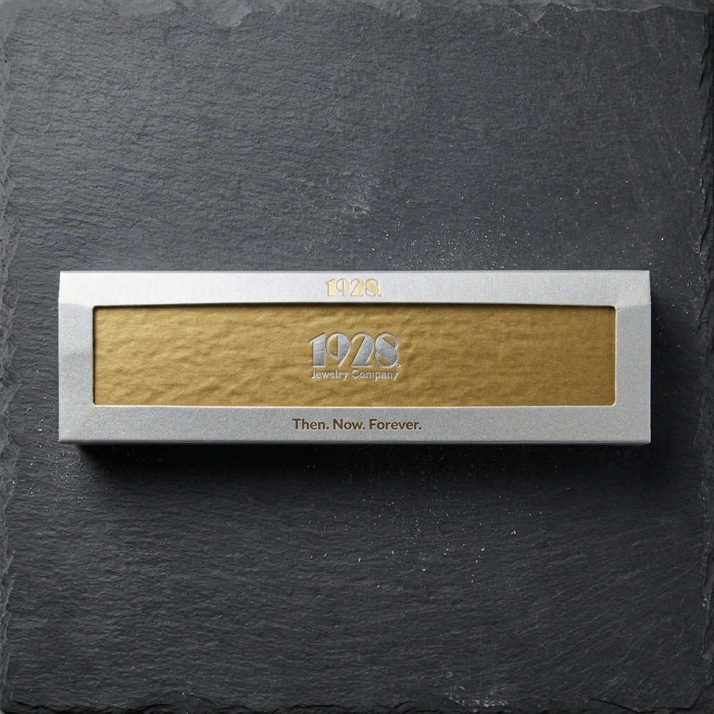 1928 Jewelry box with brand logo and "Then. Now. Forever." slogan resting on a smooth black stone surface