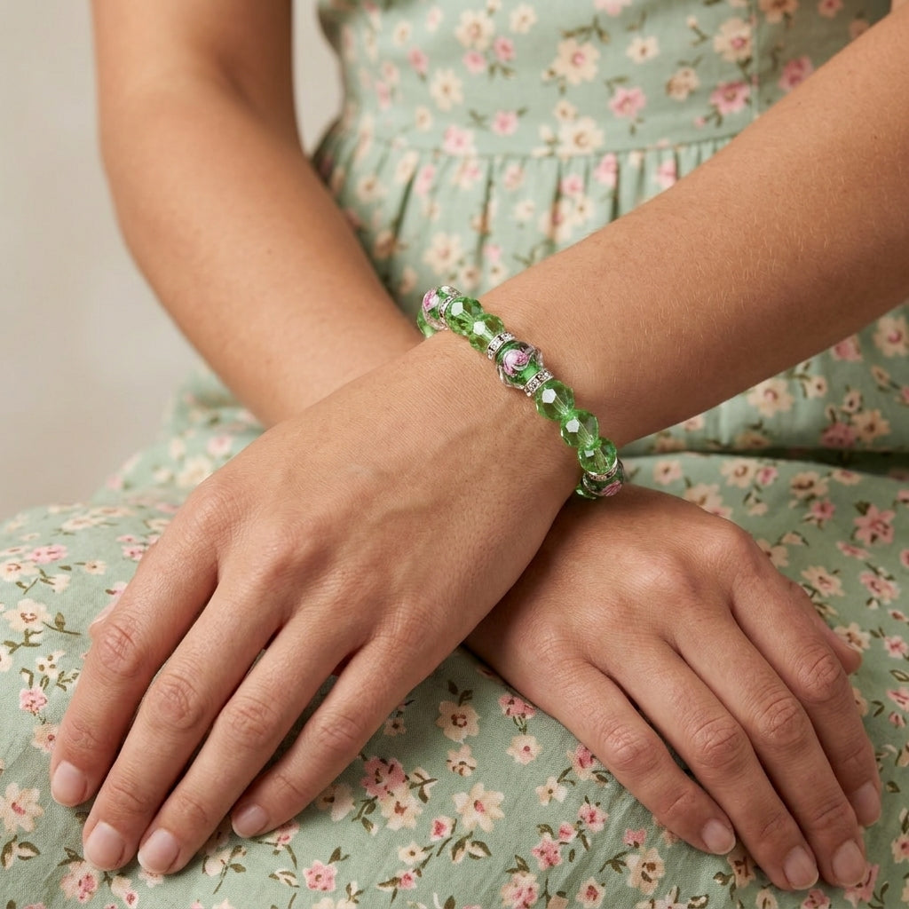 A close-up of a person wearing a green beaded bracelet with pink and white floral accents, resting their hands on their lap over a matching floral dress.