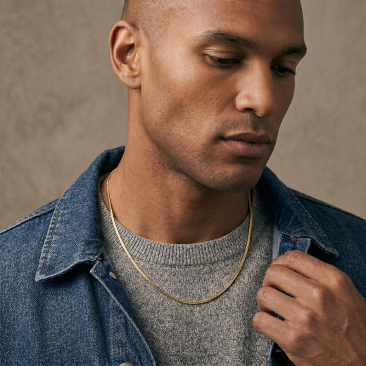 Man wearing a denim jacket over a gray sweater against a neutral background