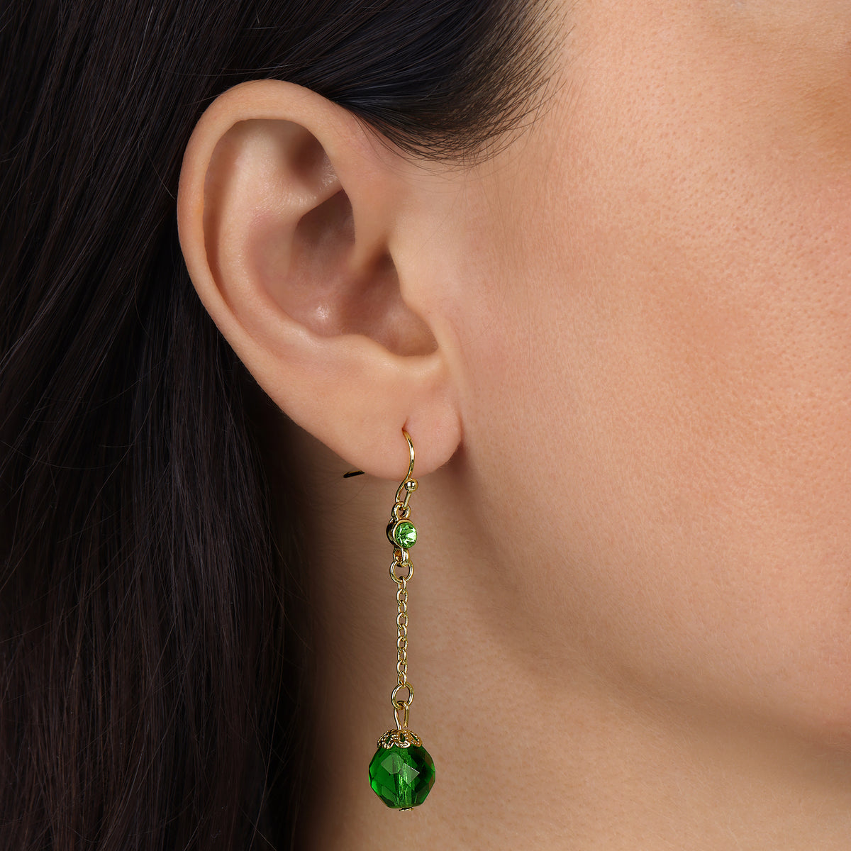A close-up of a model's ear wearing a Gold Tone Faceted Emerald Green Glass Bead & Crystal Dangle Earrings