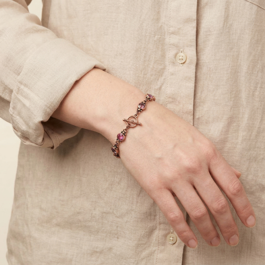 Hand wearing a bracelet with pink stones against a beige background