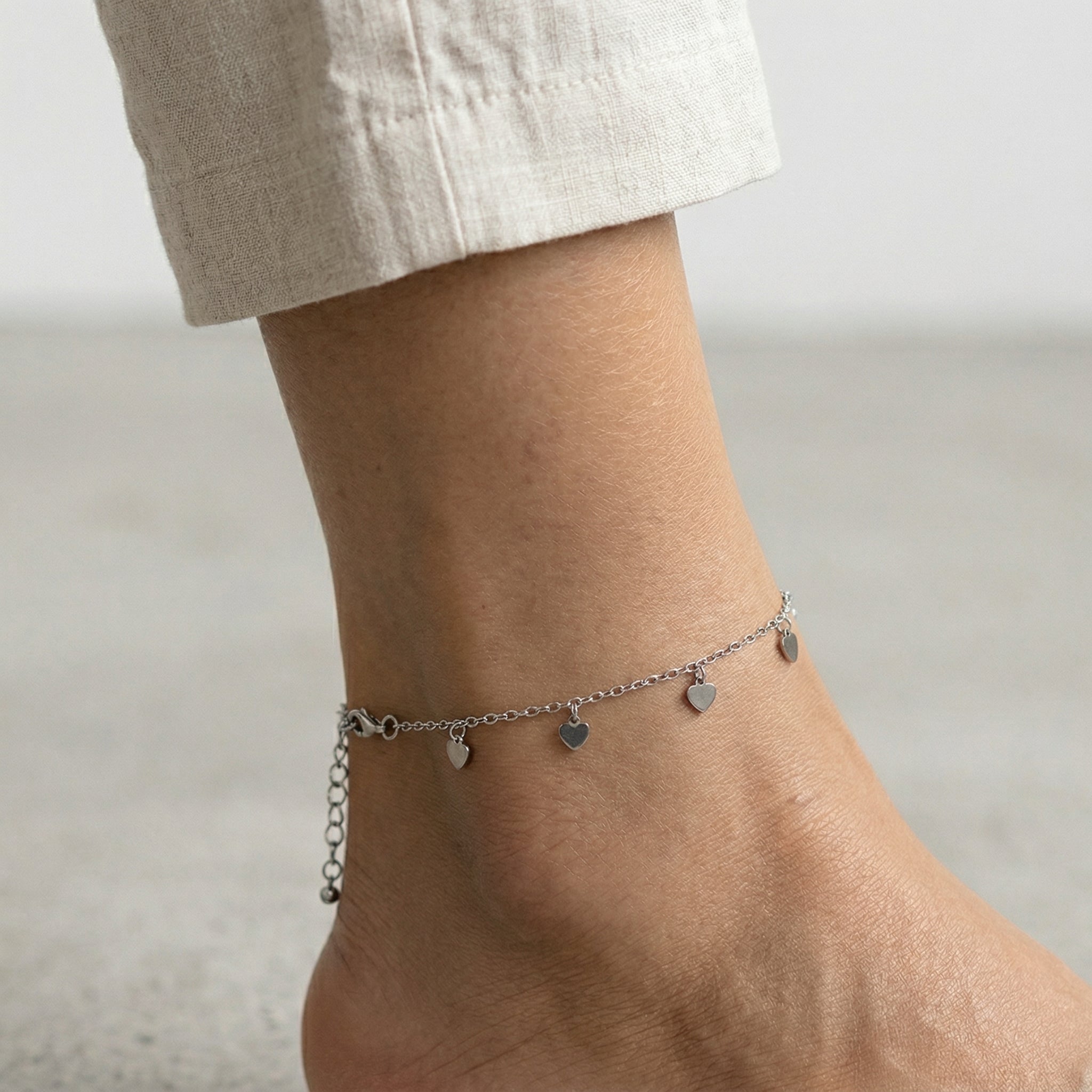 Silver tone anklet with heart charms on a woman's ankle with white linen pants