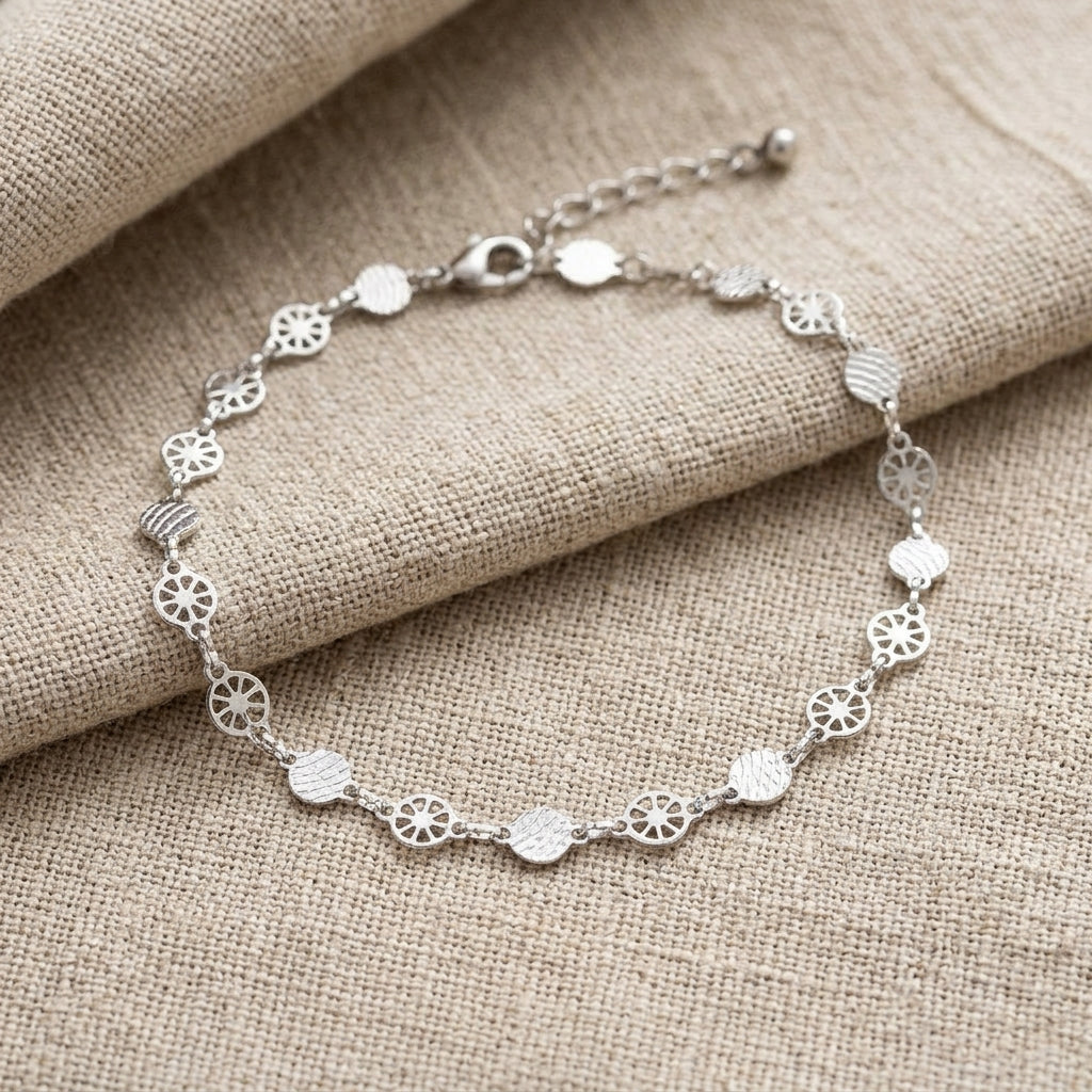 Silver anklet on a textured beige fabric background