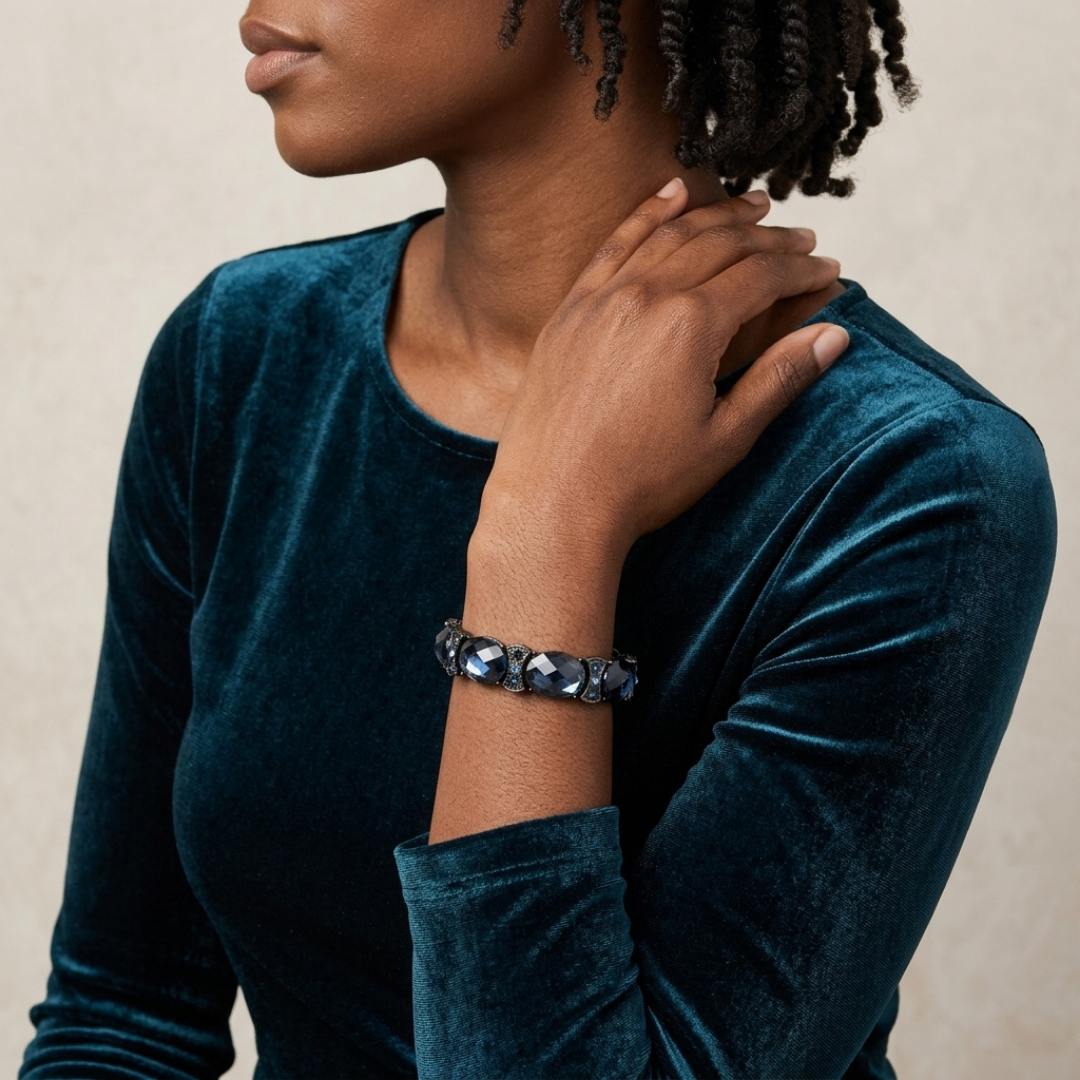 Person wearing a dark blue velvet top and a crystal bracelet on a neutral background