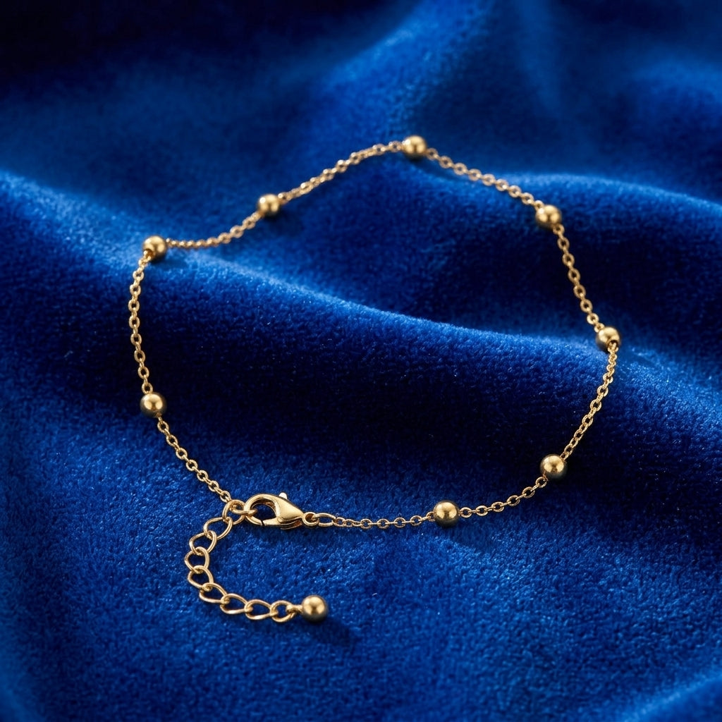 Gold tone beaded anklet on blue fabric surface