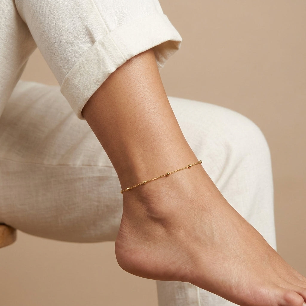 Woman in white linen pants showing off her gold tone beaded anklet