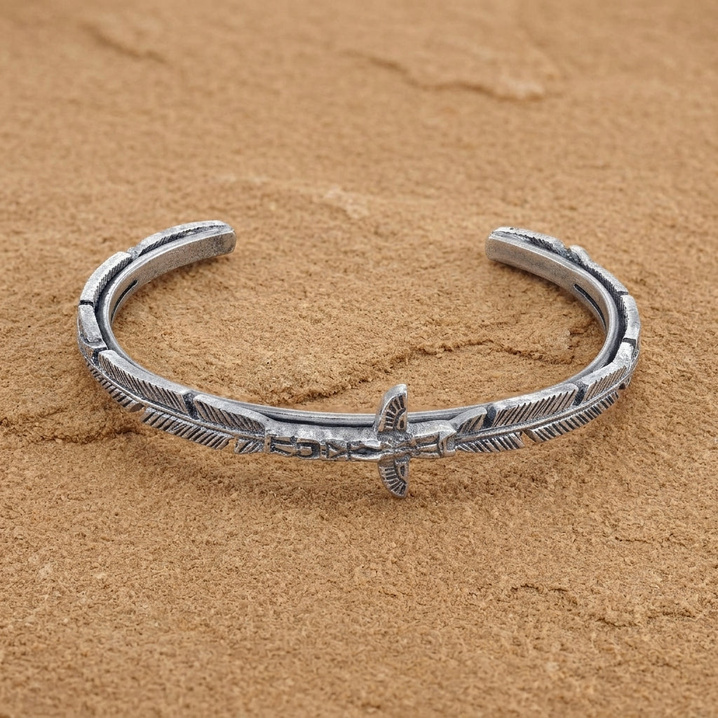 Pewter Totem Pole Feather Cuff Bracelet displayed on a textured sandy surface.