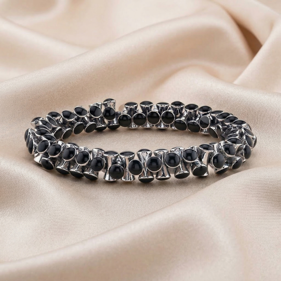 Silver bracelet with black beads on a beige fabric background