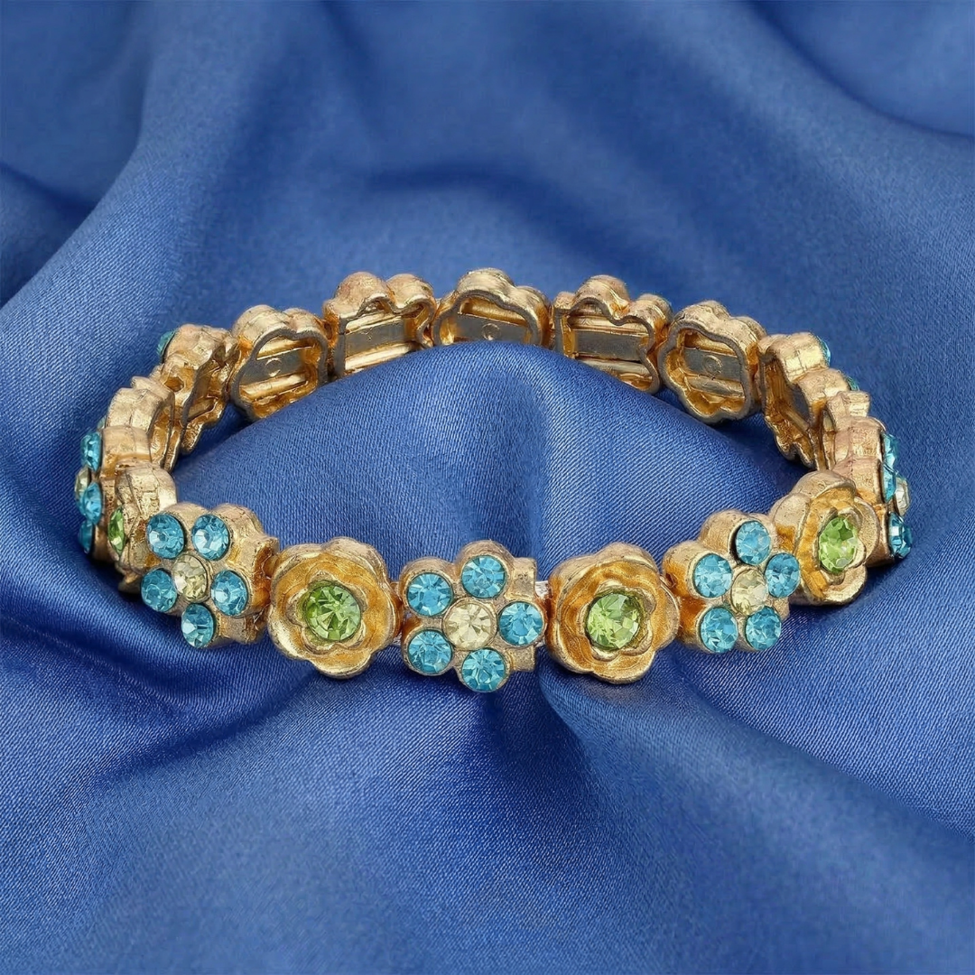 Gold bracelet with floral designs and blue and green crystals on a blue fabric background