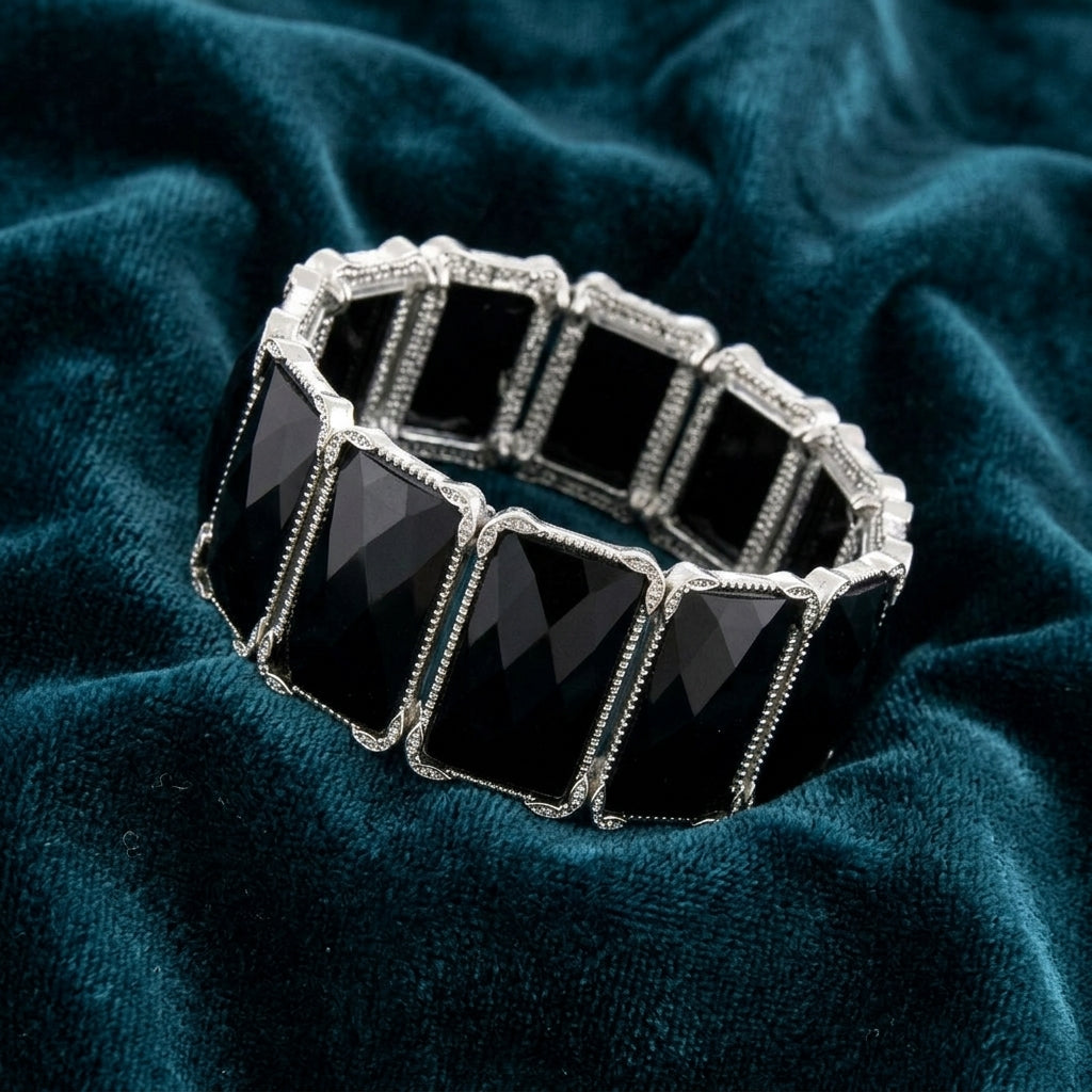 Black stone bracelet with silver tone accents resting on dark blue fabric