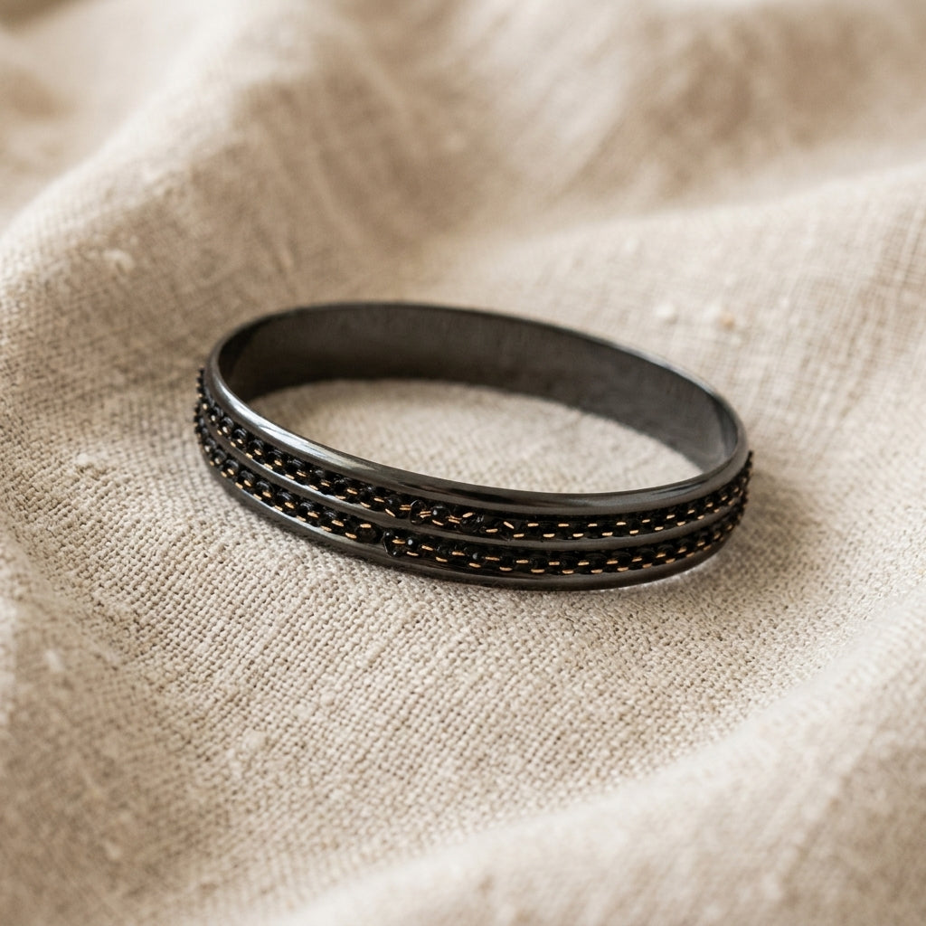 Black bracelet with gold accents on a beige fabric background