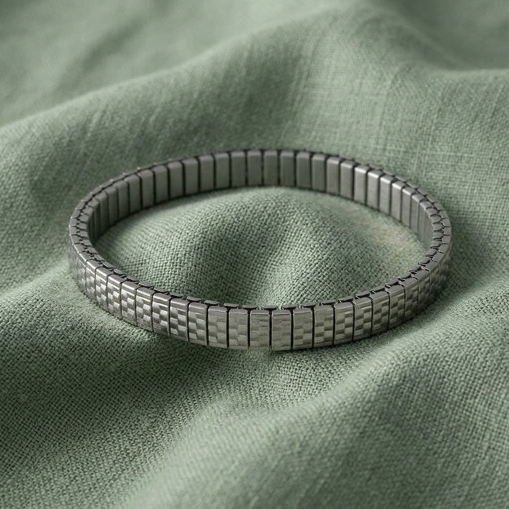 A metallic silver tone link stretch bracelet resting on a textured sage green fabric background.
