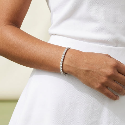 A close-up of a woman's arm and hand wearing a sparkling silver rhinestone tennis bracelet, dressed in a white top and skirt.