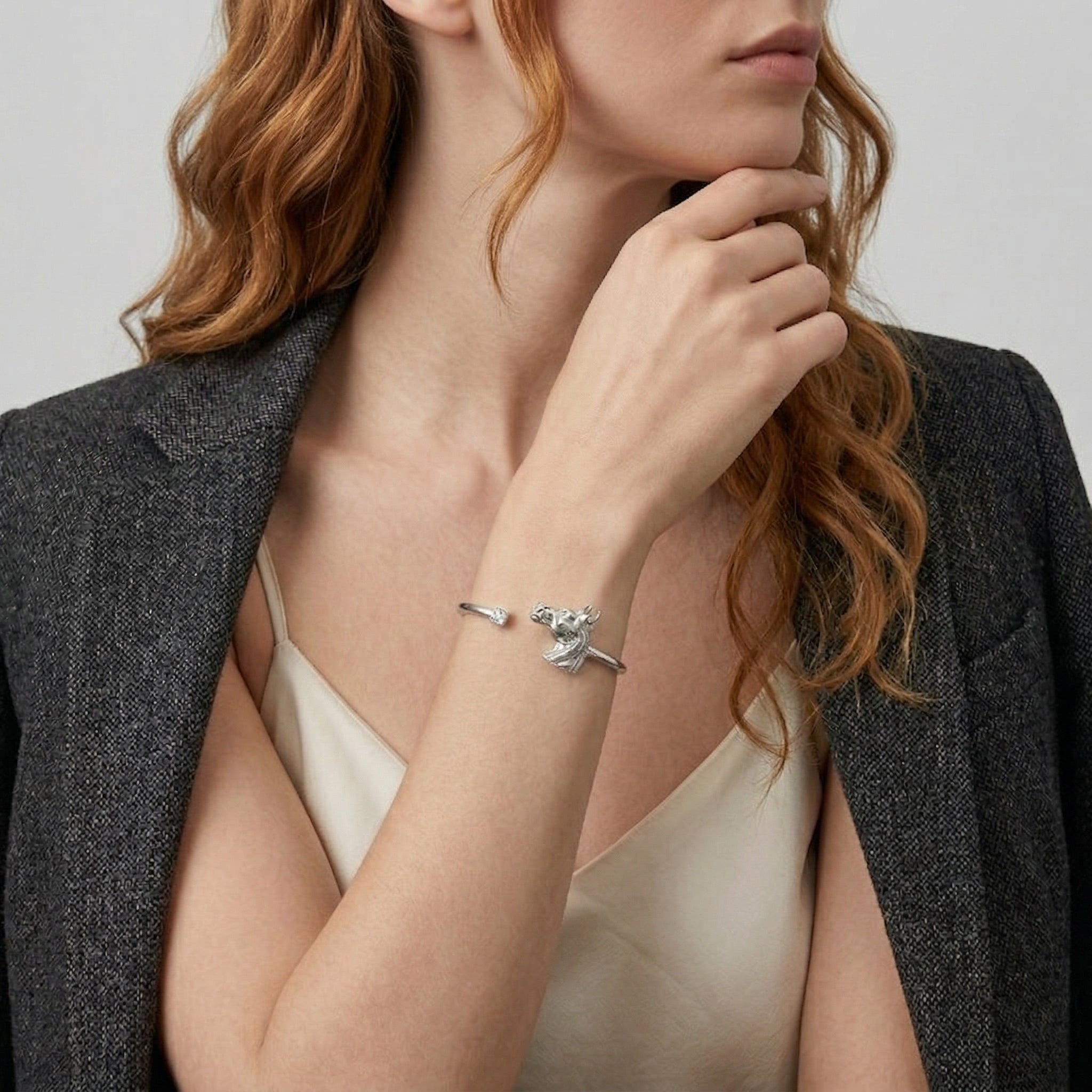 Woman wearing a silver tone horse head design spring cuff bracelet with a clear crystal accent
